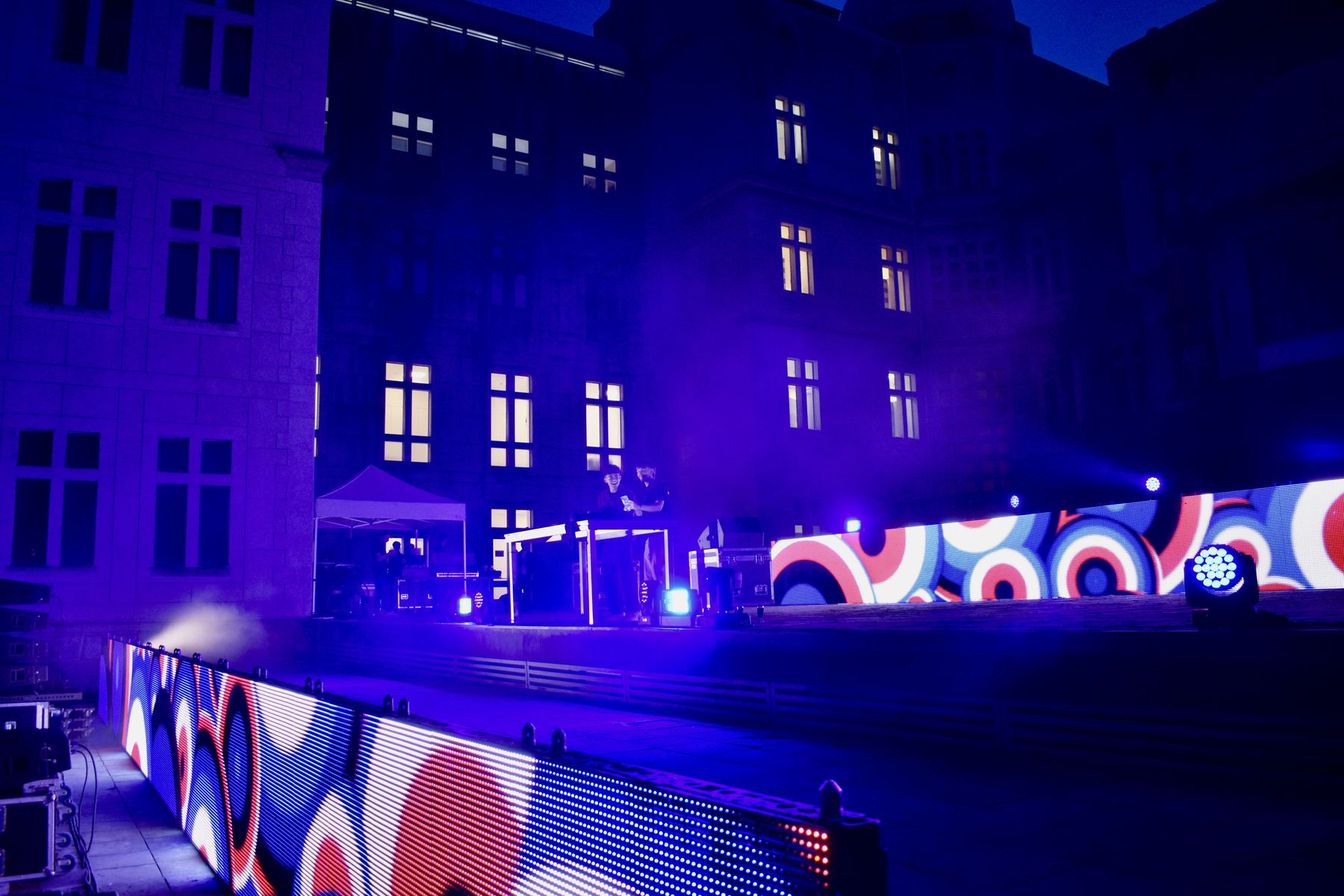 La facciata della facoltà illuminata di viola di notte, con il ledwall del palco e le luci